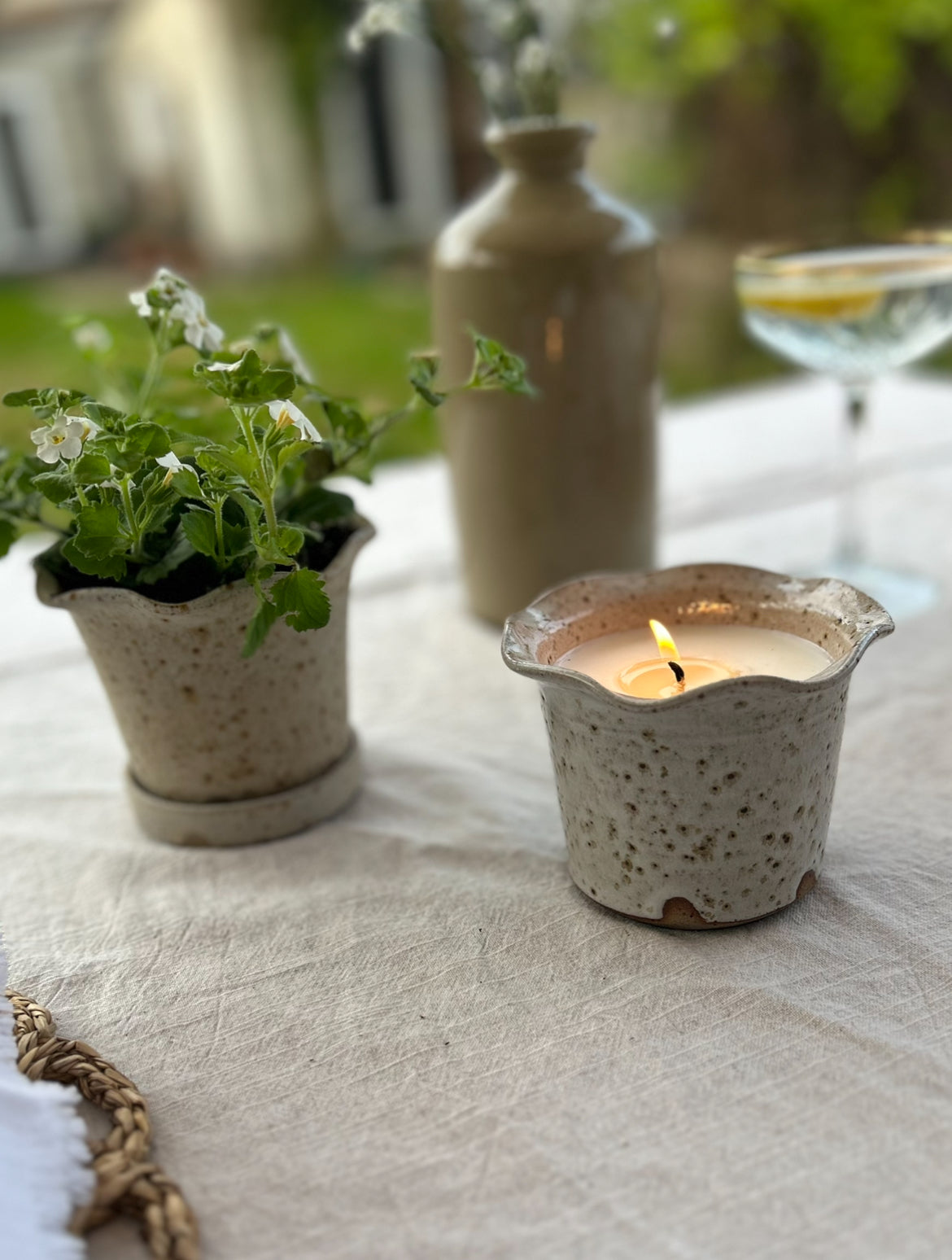 The Garden Candle stands on a table next to a plant pot