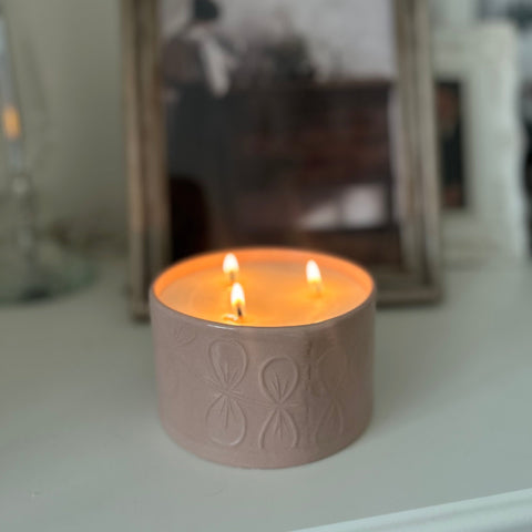 A large 3 wick refillable candle in pink is lit and on a work top