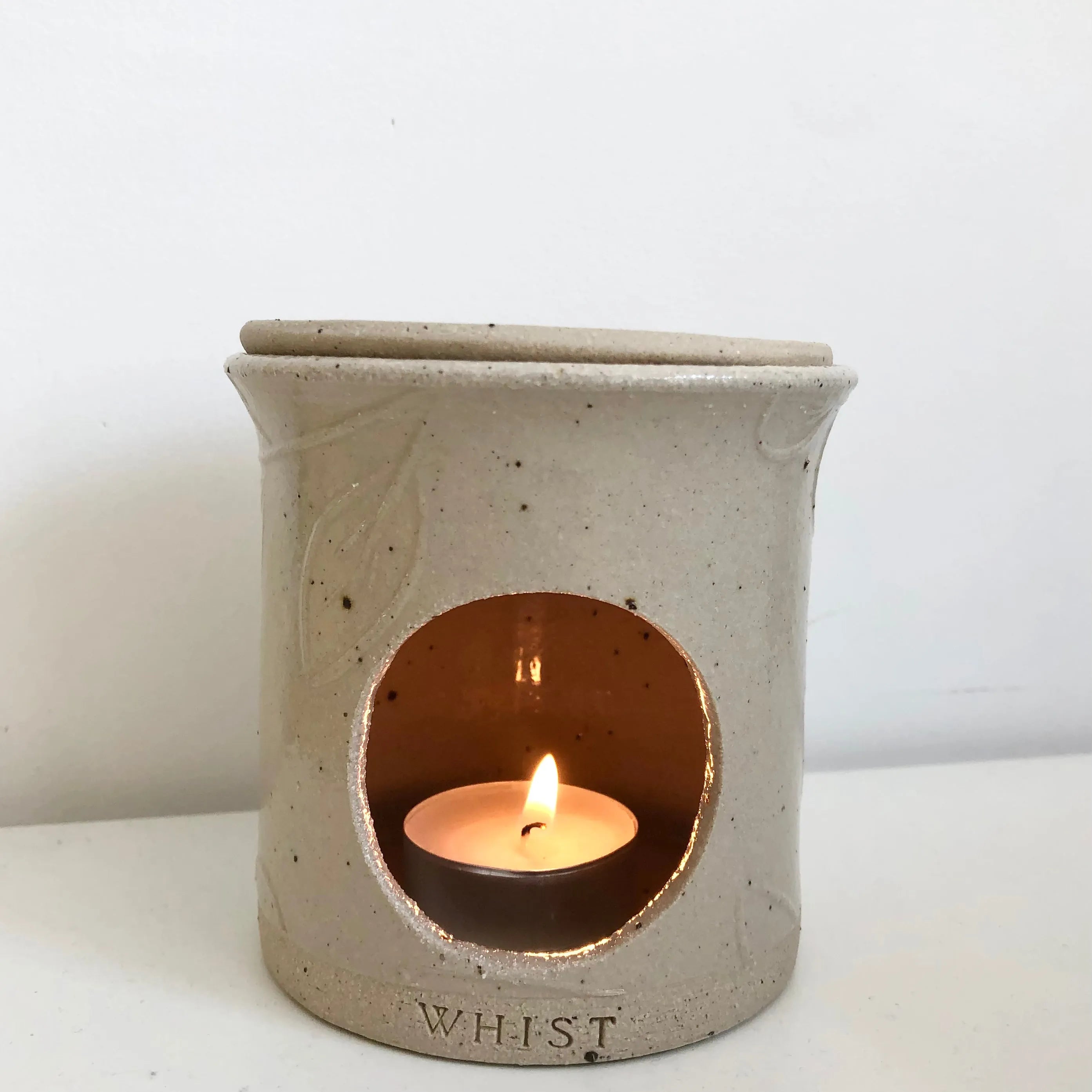a nude coloured ceramic wax melt warmer has  tealight lit within it