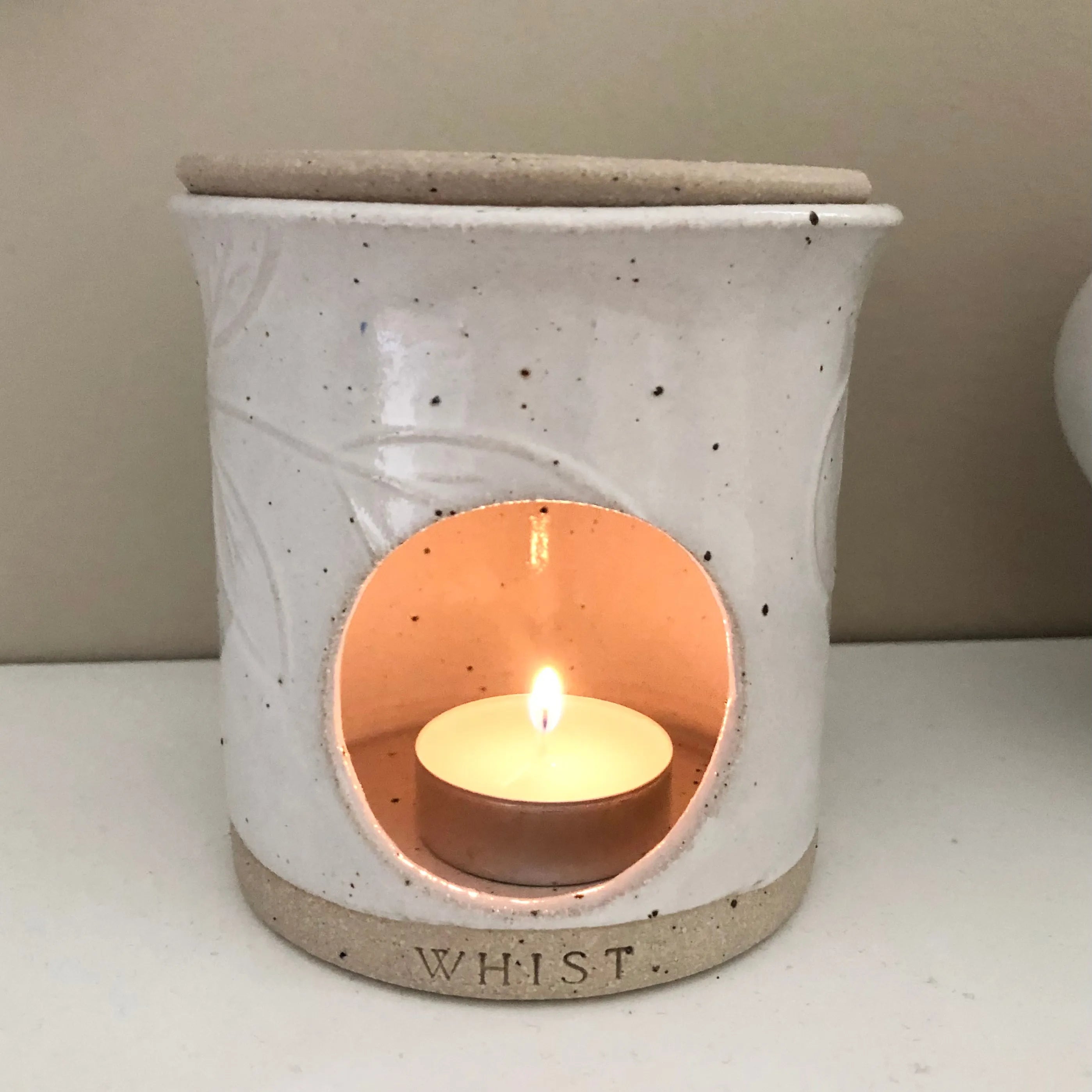 A white ceramic wax melt warmer has a lit tealight in it