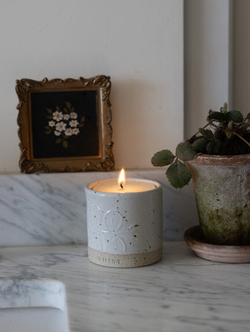 A white refillable candle is lit and on a kitchen worktop